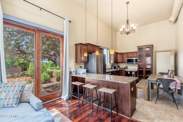 kitchen with a kitchen bar, an inviting chandelier, light wood-type flooring, stainless steel appliances, and kitchen peninsula