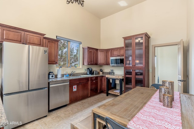 kitchen with sink, stainless steel appliances, light tile patterned flooring, and a towering ceiling