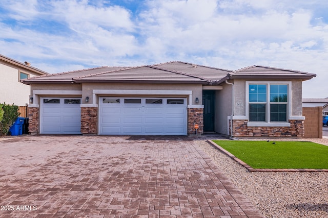 prairie-style home featuring stone siding, decorative driveway, an attached garage, and stucco siding