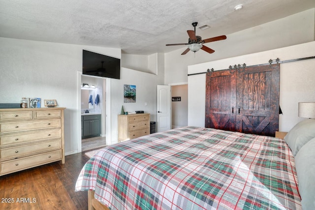 bedroom featuring ceiling fan, a barn door, dark hardwood / wood-style flooring, ensuite bathroom, and vaulted ceiling