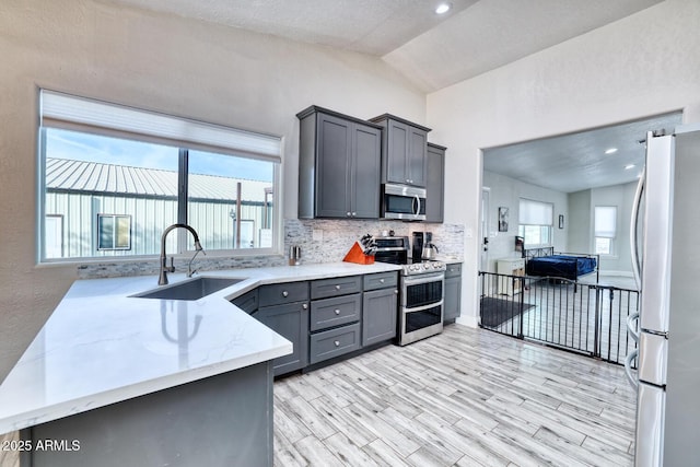 kitchen featuring kitchen peninsula, light stone countertops, stainless steel appliances, sink, and lofted ceiling