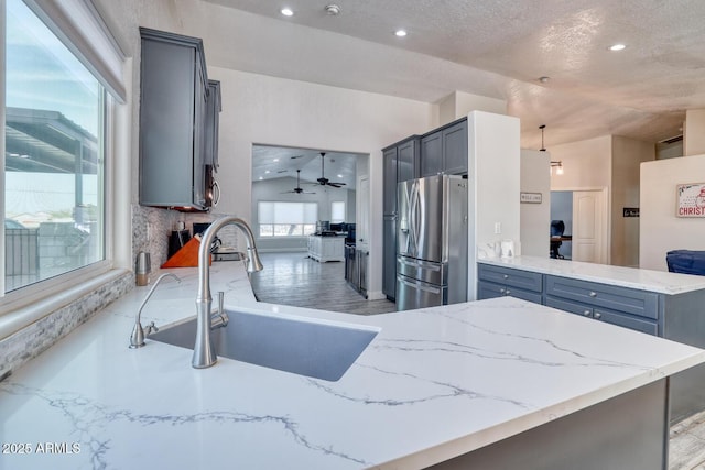 kitchen featuring kitchen peninsula, stainless steel fridge, vaulted ceiling, sink, and pendant lighting