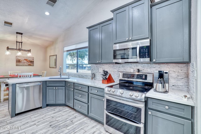 kitchen featuring sink, tasteful backsplash, lofted ceiling, gray cabinets, and appliances with stainless steel finishes