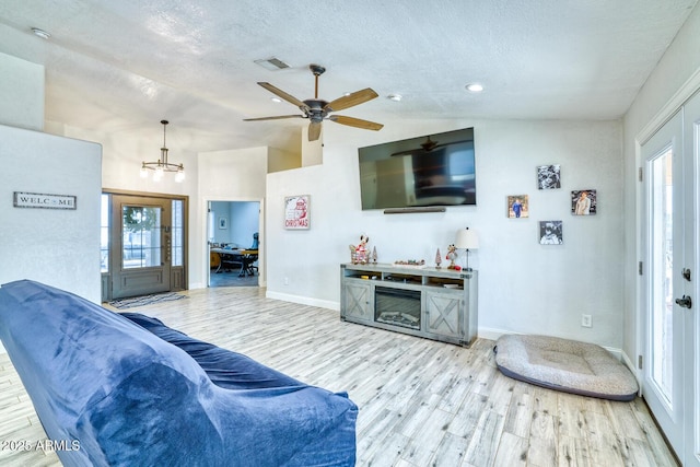 living room with a textured ceiling, light hardwood / wood-style flooring, a wealth of natural light, and lofted ceiling