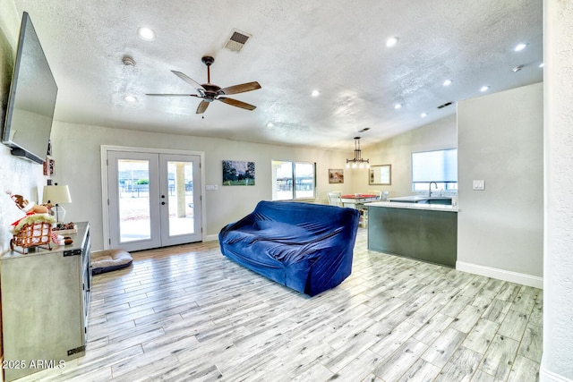 living room with french doors, ceiling fan with notable chandelier, a textured ceiling, and light hardwood / wood-style flooring