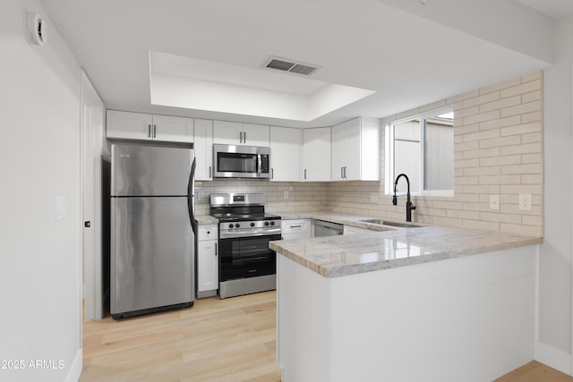 kitchen with visible vents, a peninsula, stainless steel appliances, decorative backsplash, and light wood-type flooring