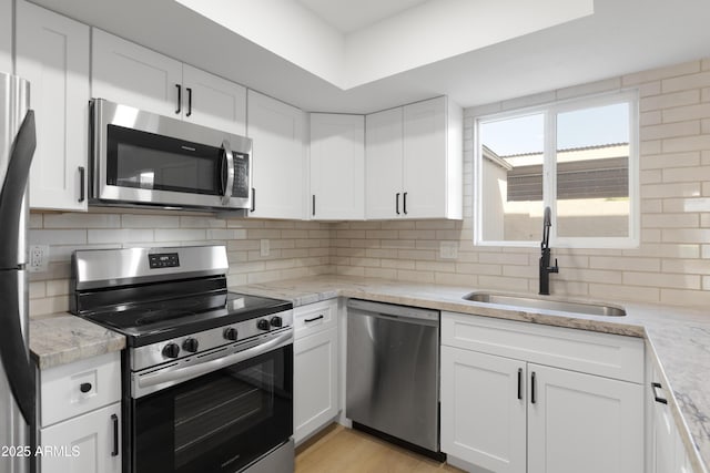 kitchen with tasteful backsplash, light wood-type flooring, white cabinets, stainless steel appliances, and a sink