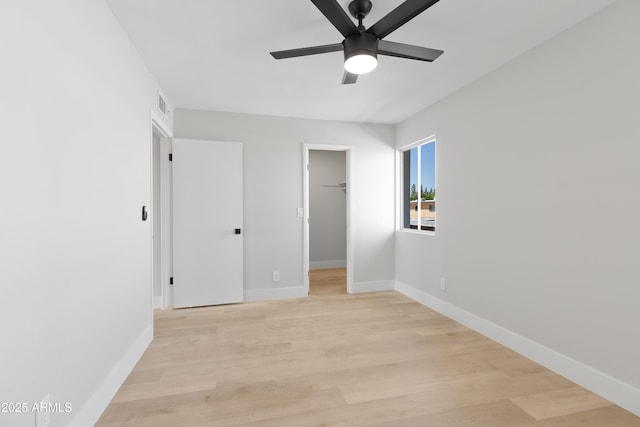 unfurnished bedroom featuring visible vents, light wood-style flooring, a walk in closet, and baseboards