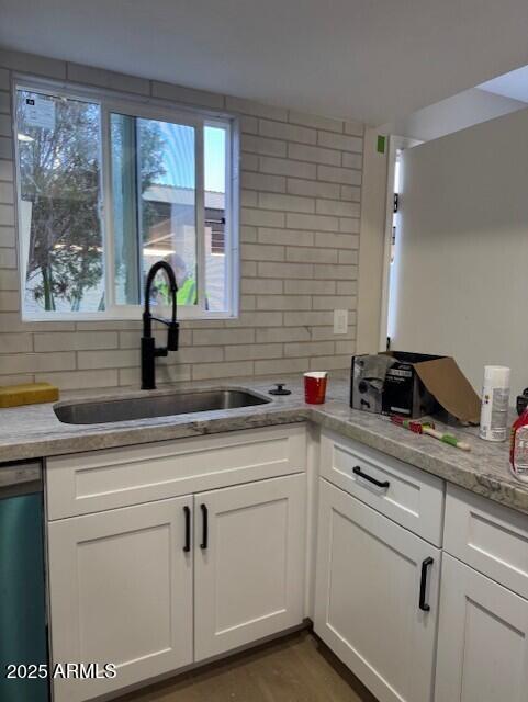 kitchen featuring light countertops, dishwashing machine, decorative backsplash, white cabinets, and a sink