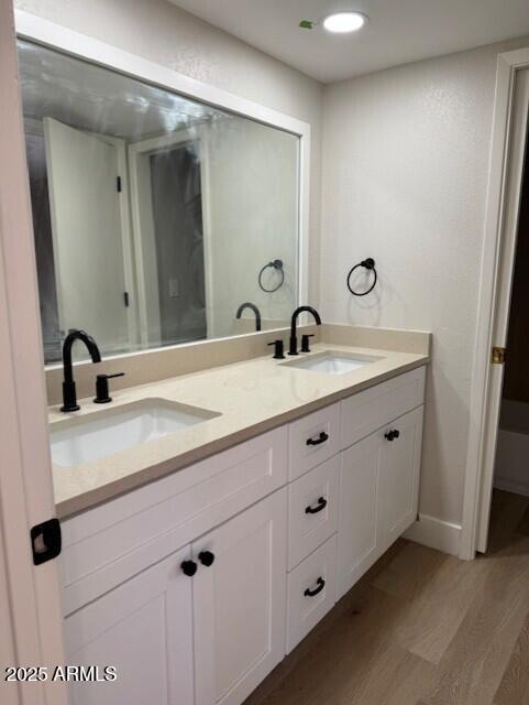 full bathroom with a sink, baseboards, wood finished floors, and double vanity