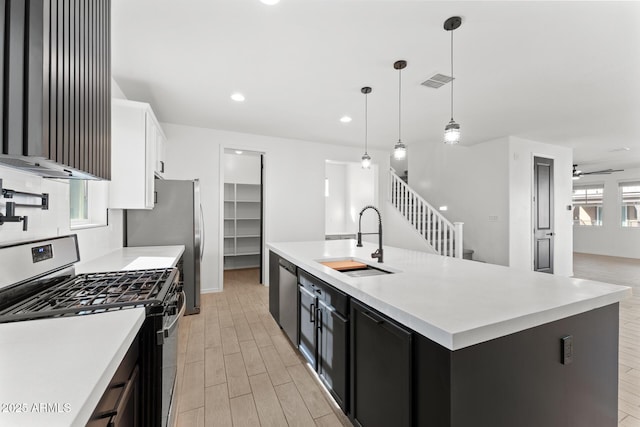 kitchen with sink, a kitchen island with sink, stainless steel appliances, white cabinets, and decorative light fixtures