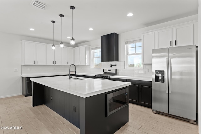 kitchen with appliances with stainless steel finishes, sink, white cabinets, hanging light fixtures, and a kitchen island with sink