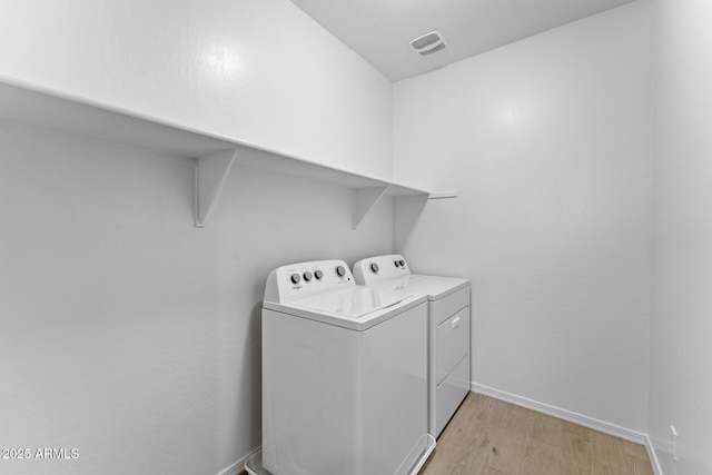 clothes washing area with washer and clothes dryer and light wood-type flooring