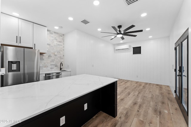 kitchen with white cabinetry, a wall mounted air conditioner, appliances with stainless steel finishes, light stone countertops, and light hardwood / wood-style floors