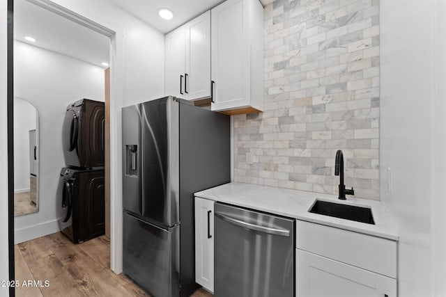 kitchen with stacked washer and dryer, stainless steel appliances, sink, and white cabinets