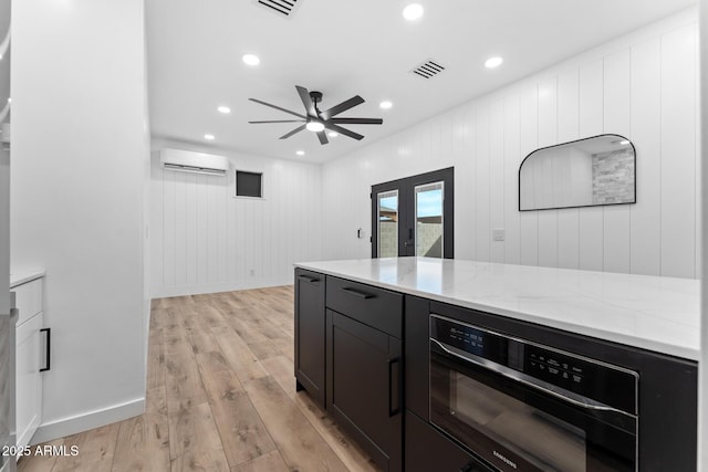 kitchen with light stone counters, ceiling fan, a wall unit AC, and light hardwood / wood-style flooring