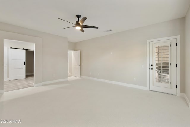 unfurnished bedroom featuring light carpet, ceiling fan, a barn door, and access to outside