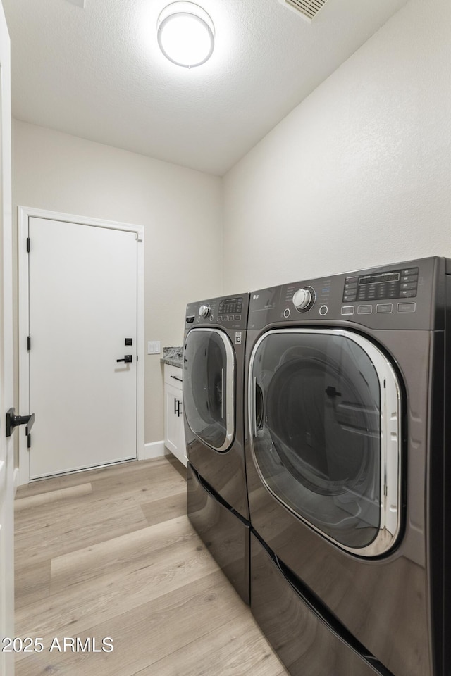 laundry area with light wood-type flooring, separate washer and dryer, and cabinets