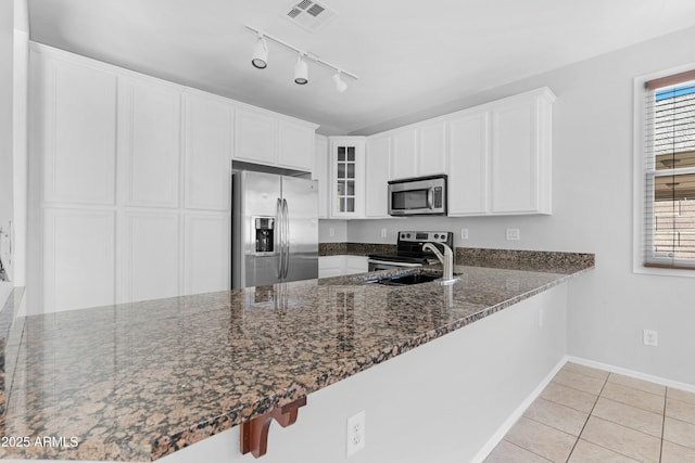 kitchen featuring glass insert cabinets, light tile patterned floors, dark stone countertops, appliances with stainless steel finishes, and a peninsula