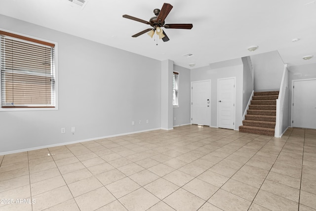 unfurnished living room featuring light tile patterned floors, baseboards, a ceiling fan, and stairs