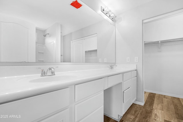 bathroom featuring baseboards, double vanity, wood finished floors, a shower, and a sink