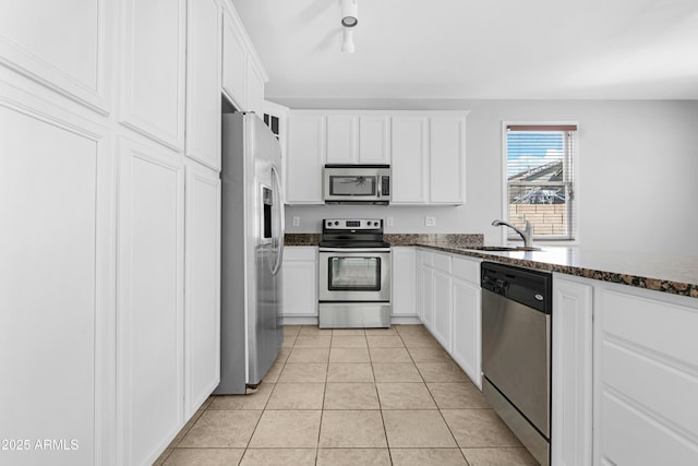 kitchen with a sink, white cabinetry, stainless steel appliances, dark stone counters, and light tile patterned floors