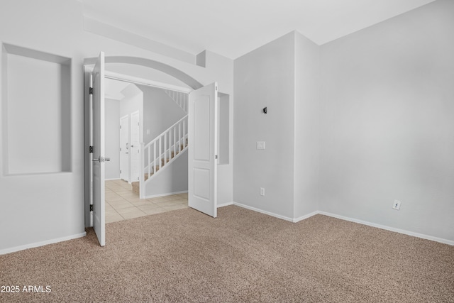 carpeted empty room featuring stairs, baseboards, and tile patterned flooring