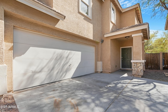 exterior space with stucco siding, an attached garage, driveway, and fence