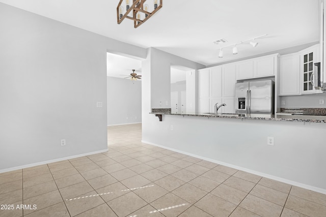 kitchen with visible vents, glass insert cabinets, ceiling fan, stainless steel fridge, and stone countertops