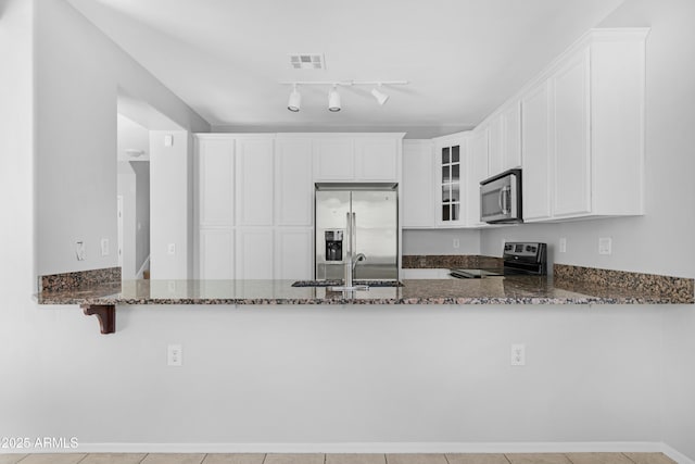 kitchen featuring glass insert cabinets, dark stone countertops, a peninsula, stainless steel appliances, and a sink