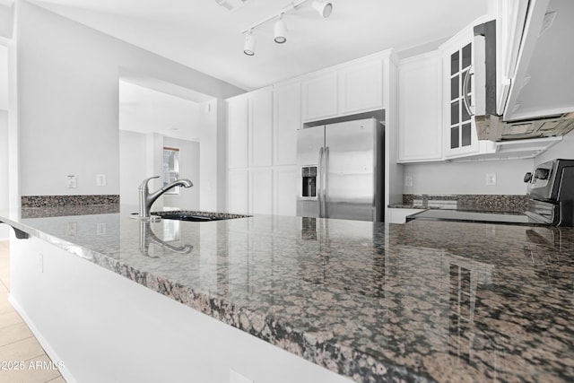 kitchen featuring dark stone counters, a sink, electric range oven, glass insert cabinets, and stainless steel refrigerator with ice dispenser