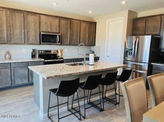 kitchen featuring light stone countertops, decorative backsplash, stainless steel appliances, and an island with sink