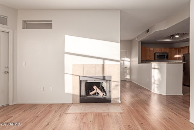 unfurnished living room featuring a tiled fireplace, light wood-style flooring, visible vents, and baseboards