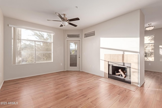 unfurnished living room featuring a tiled fireplace, light wood-style flooring, and a ceiling fan