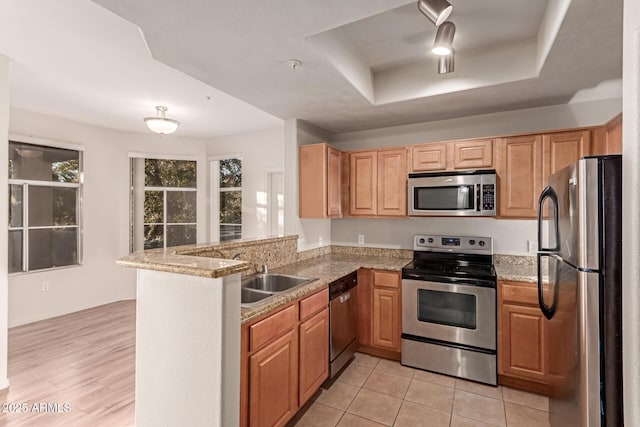 kitchen with light stone countertops, a tray ceiling, a peninsula, stainless steel appliances, and a sink