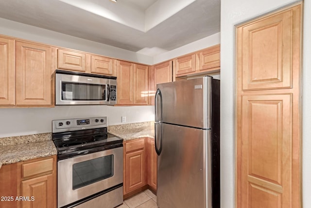 kitchen with light brown cabinetry, light tile patterned floors, stainless steel appliances, and light stone countertops