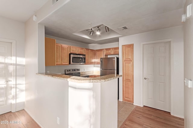 kitchen with visible vents, appliances with stainless steel finishes, a peninsula, light wood-style floors, and a raised ceiling