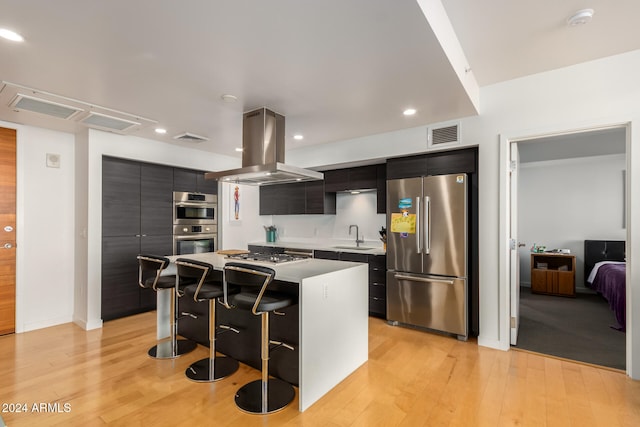 kitchen with a breakfast bar area, appliances with stainless steel finishes, a center island, island range hood, and light hardwood / wood-style floors