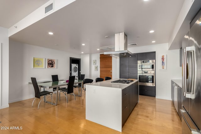 kitchen featuring stacked washer and dryer, stainless steel appliances, a kitchen island, and light hardwood / wood-style flooring