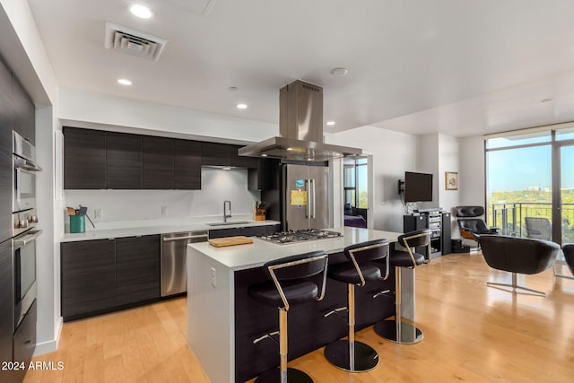 kitchen featuring sink, stainless steel appliances, a center island, island range hood, and light wood-type flooring