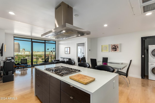 kitchen featuring light hardwood / wood-style flooring, stacked washing maching and dryer, dark brown cabinets, a center island, and island range hood