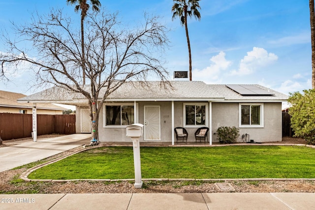 ranch-style house with a shingled roof, fence, roof mounted solar panels, a front lawn, and stucco siding