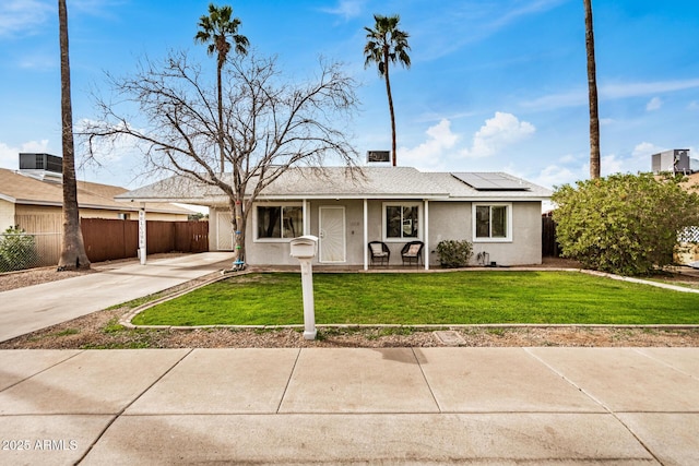 ranch-style home featuring driveway, fence, roof mounted solar panels, a front lawn, and stucco siding