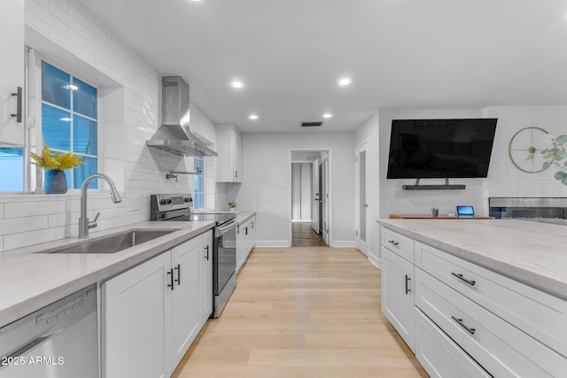 kitchen featuring white cabinets, stainless steel appliances, light stone countertops, wall chimney exhaust hood, and sink