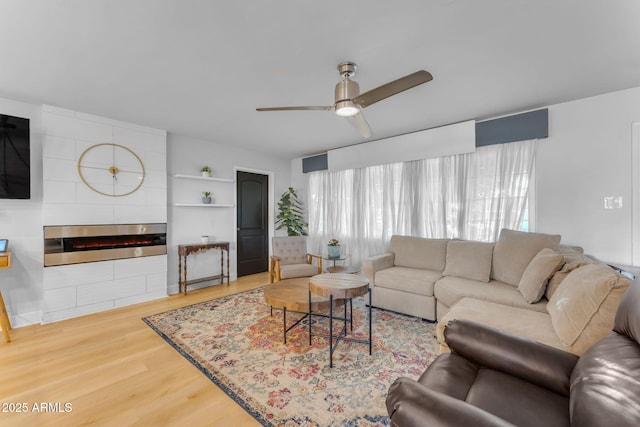 living room featuring ceiling fan, a large fireplace, and hardwood / wood-style flooring