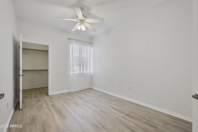 unfurnished bedroom featuring a closet, a spacious closet, baseboards, and wood finished floors