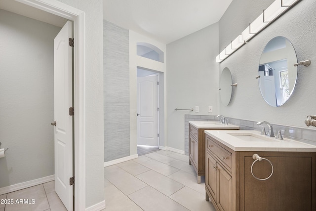 bathroom featuring tile patterned flooring, baseboards, two vanities, and a sink