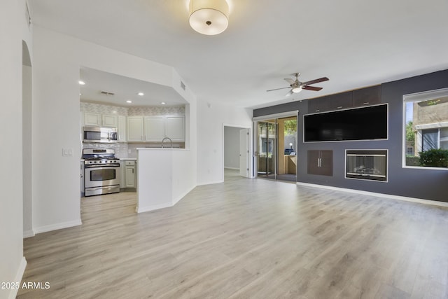 unfurnished living room featuring a glass covered fireplace, a healthy amount of sunlight, and light wood finished floors