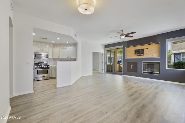 unfurnished living room featuring visible vents, a ceiling fan, baseboards, light wood-type flooring, and a glass covered fireplace