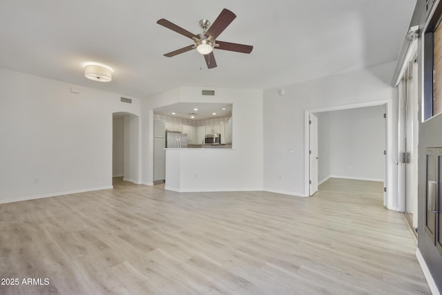 unfurnished living room with baseboards, visible vents, arched walkways, a ceiling fan, and light wood-style flooring